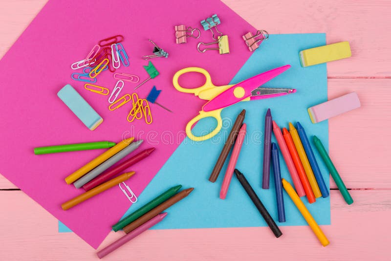 Back to school concept - school supplies: markers, crayons, pink and blue paper, scissors, eraser and other accessories on pink wooden table