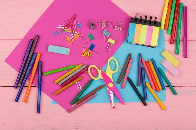 Back to school concept - school supplies: markers, crayons, pink and blue paper, scissors, eraser and other accessories on pink wooden table