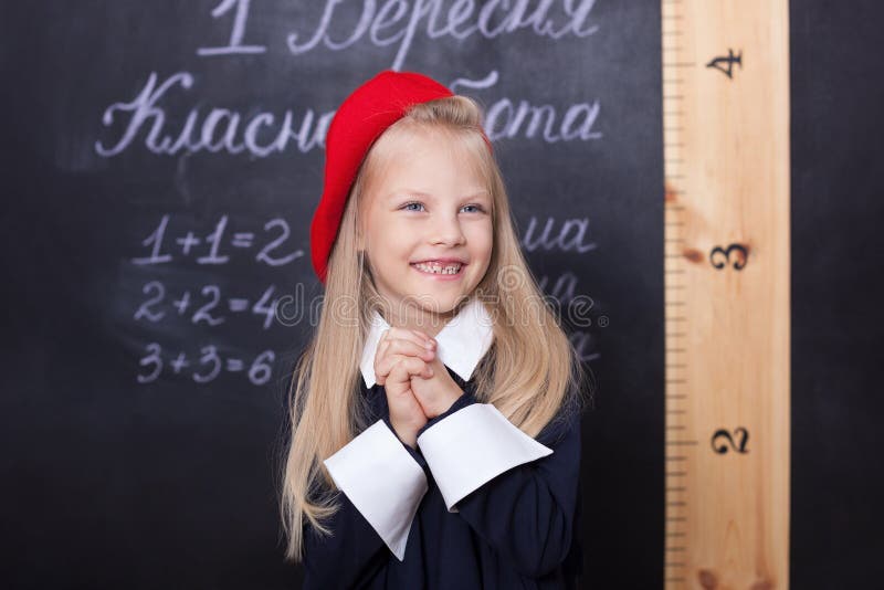 Back to school! A schoolgirl stands at the blackboard with a ruler. A schoolgirl answers the lesson. A first-grader near a chalk. Clock, happy.