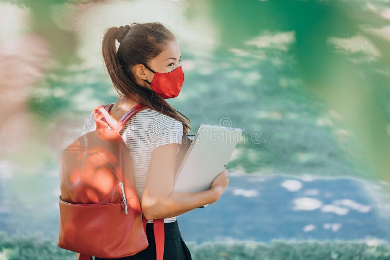 Back to school university student Asian woman wearing face mask on campus walking with red backpack, books and laptop stock image Back to school university student Asian woman wearing face mask on campus walking with red backpack, books and laptop stock image