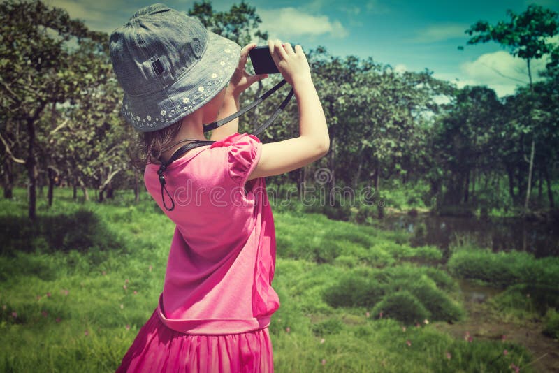 Back view of asian girl with camera at national park . Child relaxing outdoors with bright sunlight at the day time, travel on vacation. Vintage effect and cream tone. Back view of asian girl with camera at national park . Child relaxing outdoors with bright sunlight at the day time, travel on vacation. Vintage effect and cream tone.