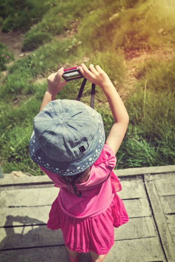 Back view of asian girl with camera at national park . Child relaxing outdoors with bright sunlight at the day time, travel on vacation. Vintage effect and cream tone. Back view of asian girl with camera at national park . Child relaxing outdoors with bright sunlight at the day time, travel on vacation. Vintage effect and cream tone.