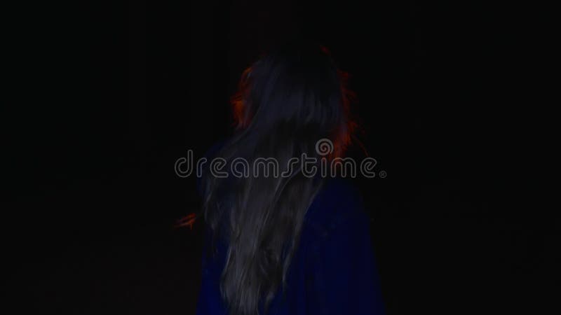 Back view of girl holding oil lamp and walking in dark forest at night