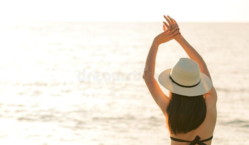Back view of happy young Asian woman in black bikini and straw hat relax and enjoy at tropical paradise beach at sunset. Girl stock image Back view of happy young Asian woman in black bikini and straw hat relax and enjoy at tropical paradise beach at sunset. Girl stock image