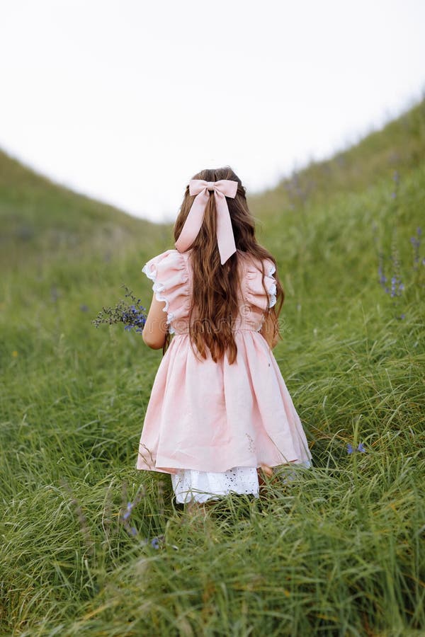 Back view of little child girl with long hair decorated silk hair bow wearing stylish pink vintage dress with lace