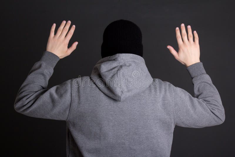 Back View of Man in Black Mask Holding Hands Up Over Grey Stock Photo