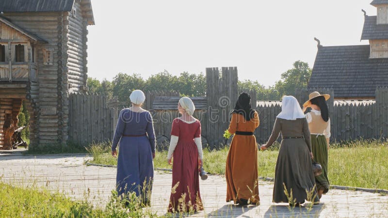 Back view of medieval women going on camera at wooden fortress background. Clothes of medieval woman of 14-15 century.