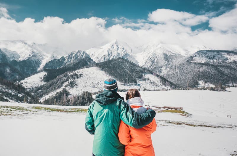 Back view photo of young loving couple hugging over winter mountains. Looking at mountains