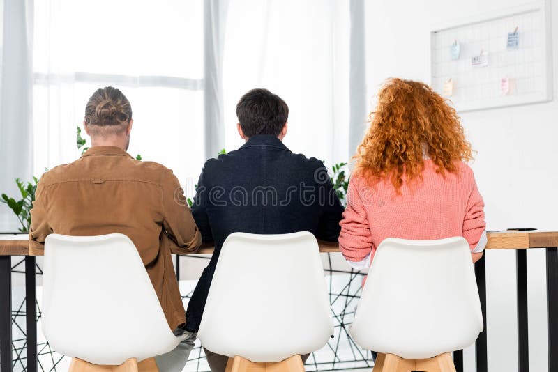 View of three friends sitting in chairs in office royalty free stock photography