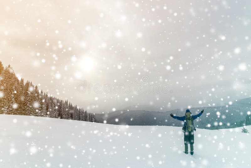 Back view of tourist hiker in warm clothing with backpack standing with raised arms on clearing covered with snow on spruce forest royalty free stock photography Back view of tourist hiker in warm clothing with backpack standing with raised arms on clearing covered with snow on spruce forest royalty free stock photography