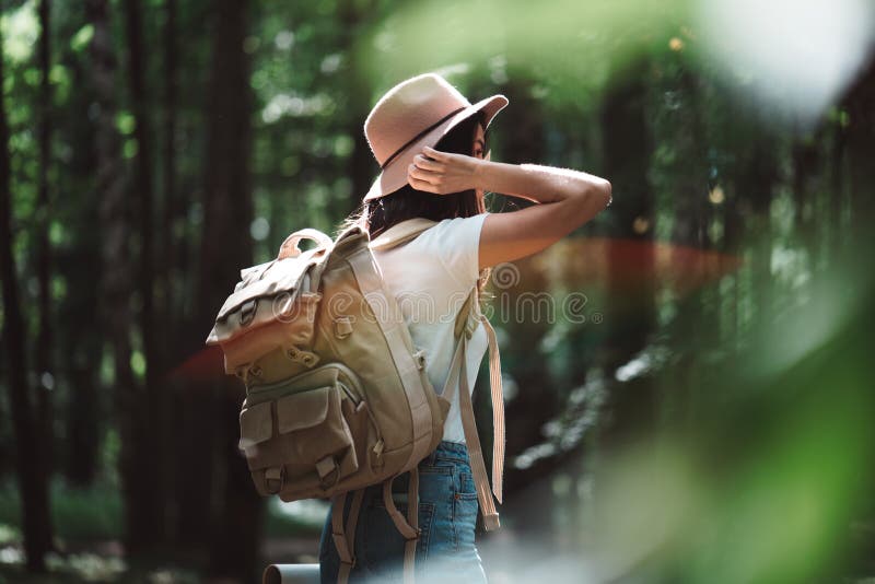 Back view on traveler backpack and hipster girl wearing hat. Young brave woman traveling alone among trees in forest on outdoors stock image Back view on traveler backpack and hipster girl wearing hat. Young brave woman traveling alone among trees in forest on outdoors stock image