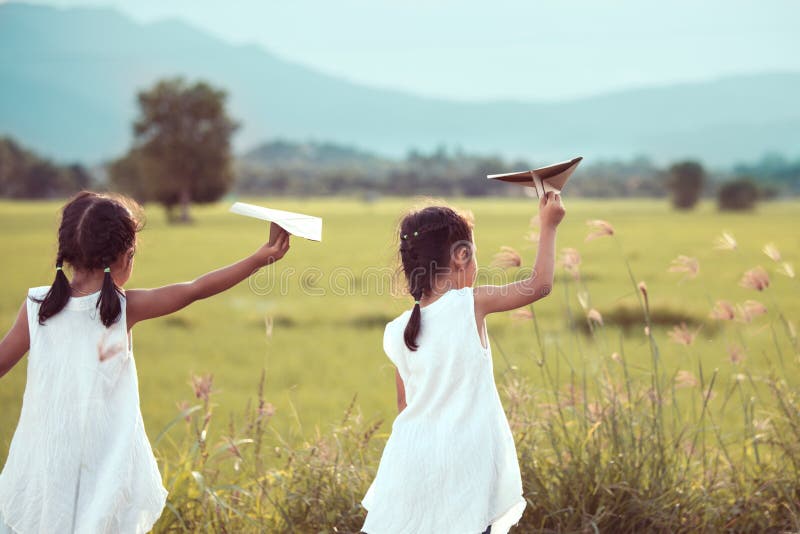 Back view of two asian child girls playing toy paper airplane
