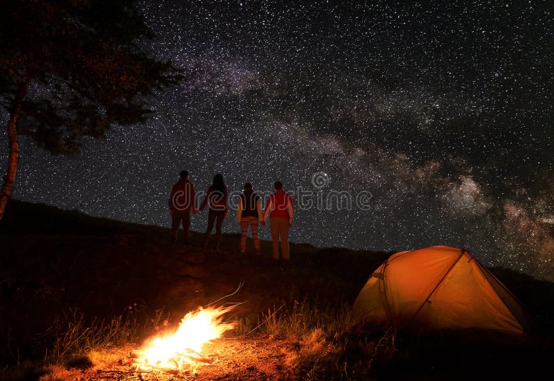 Back view of two pair holding hands and enjoying the milky way at starry sky during night of camping