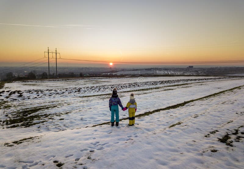 Back view of two young children in warm clothing standing in frozen snow field holding hands on copy space background of setting royalty free stock images Back view of two young children in warm clothing standing in frozen snow field holding hands on copy space background of setting royalty free stock images