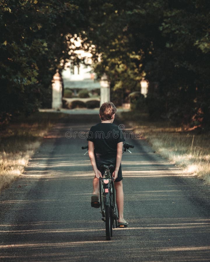 Back View of a Young Boy Riding a Bicycle with No Hands on the Forest