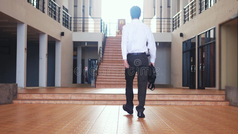 Back of view of young businessman in a suit walks with a briefcase in a business centre.