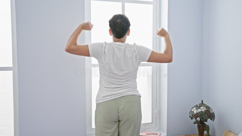 Back view of a young man stretching in a bright bedroom with a lamp and window stock image