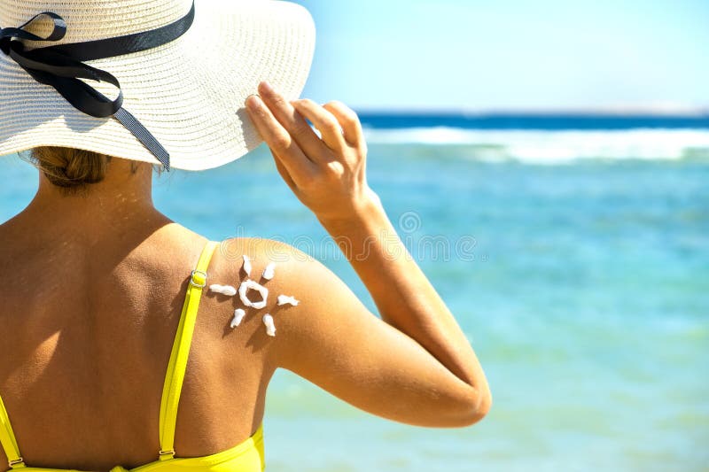 Back View Of Young Woman Tanning At The Beach With Sunscreen Cream In Sun Shape On Her Shoulder 