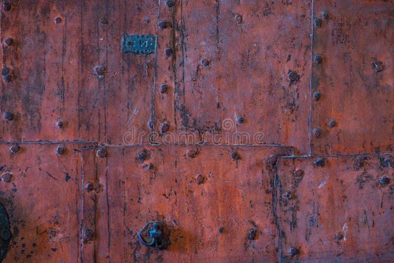 Old damaged grunge decorated faded reddish brown historic wooden door with bolts, handles and latch background