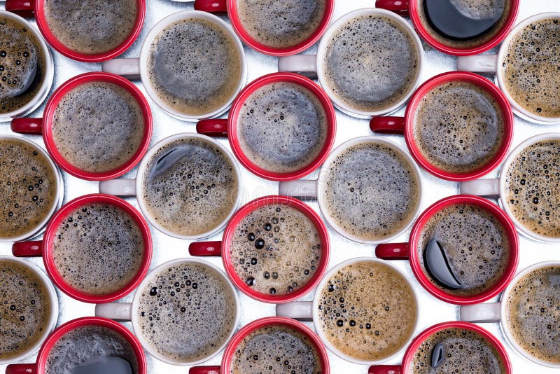 Background pattern of red and white coffee mugs arranged in alternate rows filled with frothy freshly brewed and poured black coffee viewed from above on a metal surface