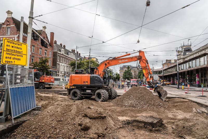 Backhoe som reparerar spårvagnspåren i gatorna av Amsterdam om den molniga och regniga dagen fotografering för bildbyråer Backhoe som reparerar spårvagnspåren i gatorna av Amsterdam om den molniga och regniga dagen fotografering för bildbyråer