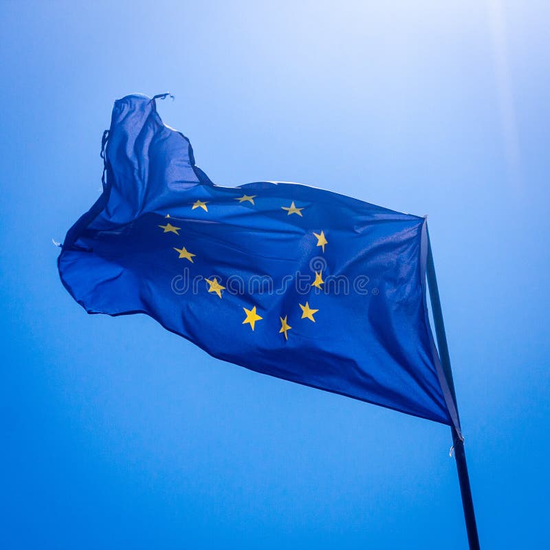 A ragged European Union flag backlit against a deep blue sky. A ragged European Union flag backlit against a deep blue sky