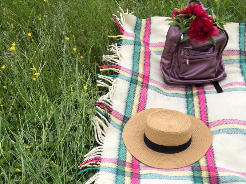 A Backpack with Red Peonies Inside and a Straw Hat on the Checkered