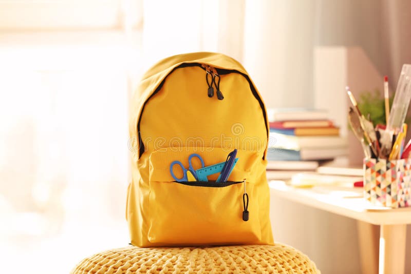 Backpack with school supplies on pouf royalty free stock image