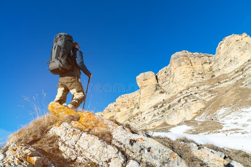 Backpacker with a Large Backpack and Sticks Ascends To the Rock on