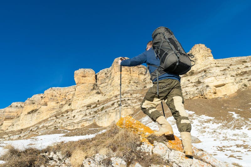 Backpacker with a Large Backpack and Sticks Ascends To the Rock on