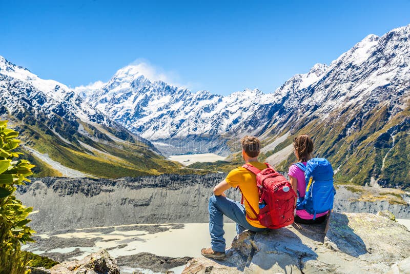 Backpackers couple hiking looking at Mount Cook view on mountains tramping in New Zealand. People hikers relaxing during