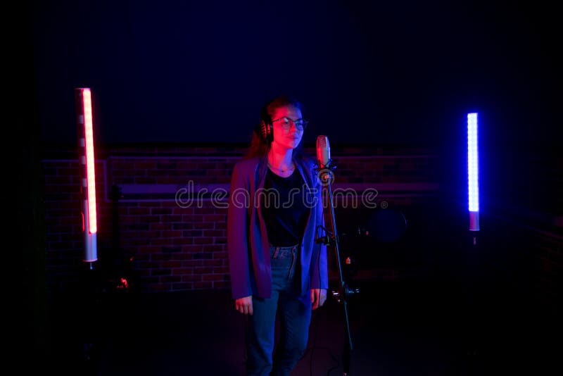 backstage Une jeune femme en verres se tenant pr?t le microphone dans l'?clairage au n?on photo stock backstage Une jeune femme en verres se tenant pr?t le microphone dans l'?clairage au n?on photo stock