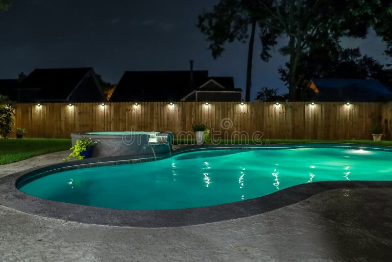 A backyard swimming pool and jacuzzi hot tob at night