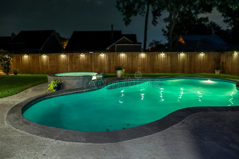 A backyard swimming pool and jacuzzi hot tob at night