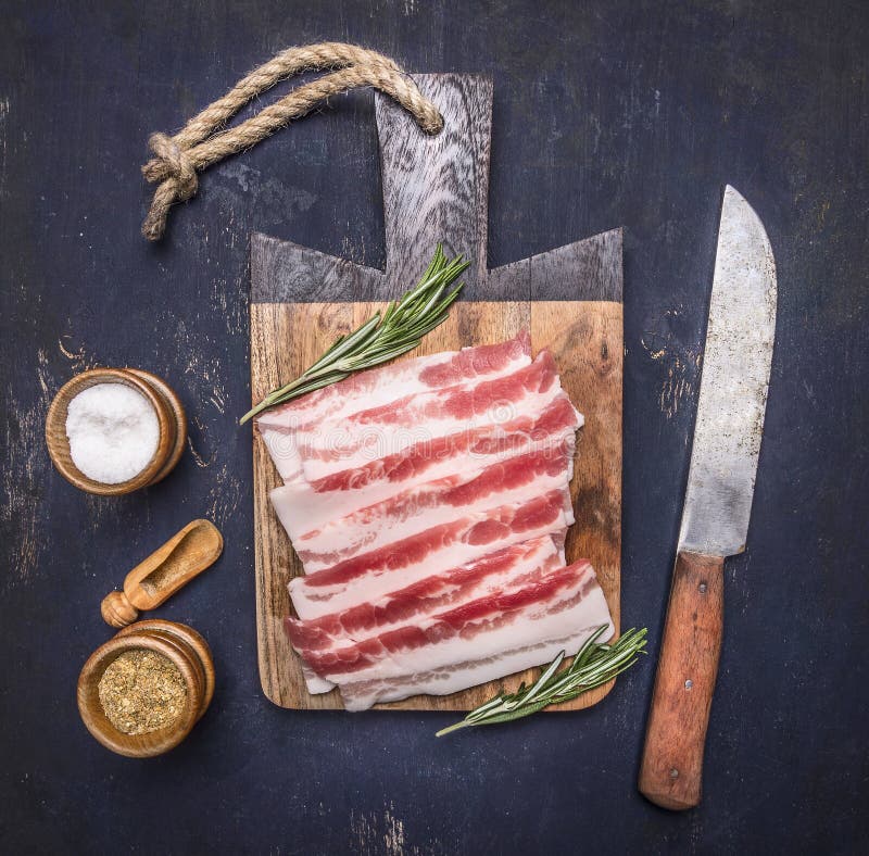 Bacon, alecrins, faca e especiarias crus deliciosos em um fim rústico de madeira da opinião superior do fundo da placa de corte a
