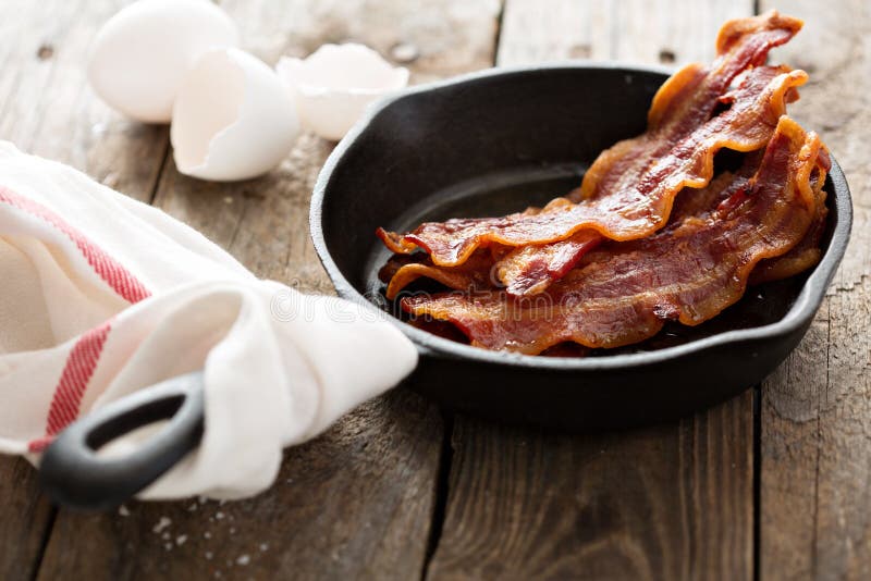 Bacon quente crepitante em um frigideira do ferro fundido imagem de stock Bacon quente crepitante em um frigideira do ferro fundido imagem de stock