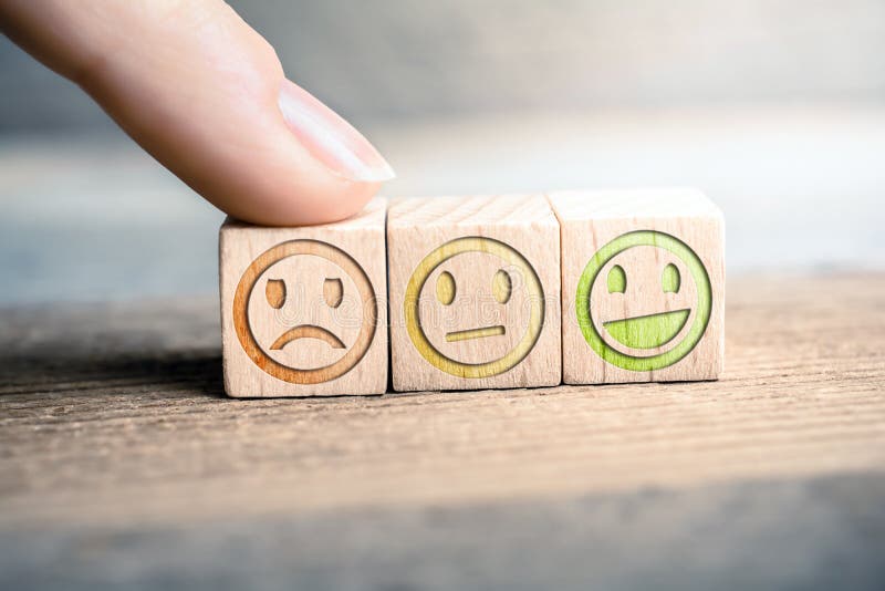 Bad Feedback Concept With Red, Yellow And Green Smiling Faces On Blocks On A Wooden Board, The Red Face Is Touched By A Finger. Bad Feedback Concept With Red, Yellow And Green Smiling Faces On Blocks On A Wooden Board, The Red Face Is Touched By A Finger