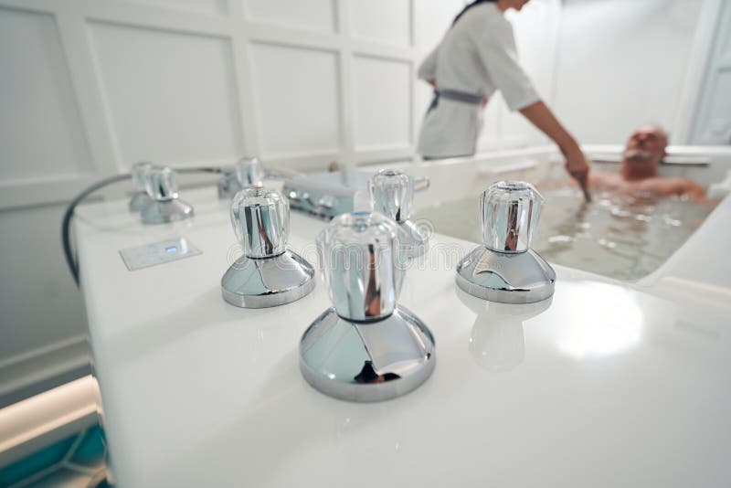 Close up of male person lying in bathtub with metal thermostatic parts while having hydromassage procedure. Close up of male person lying in bathtub with metal thermostatic parts while having hydromassage procedure