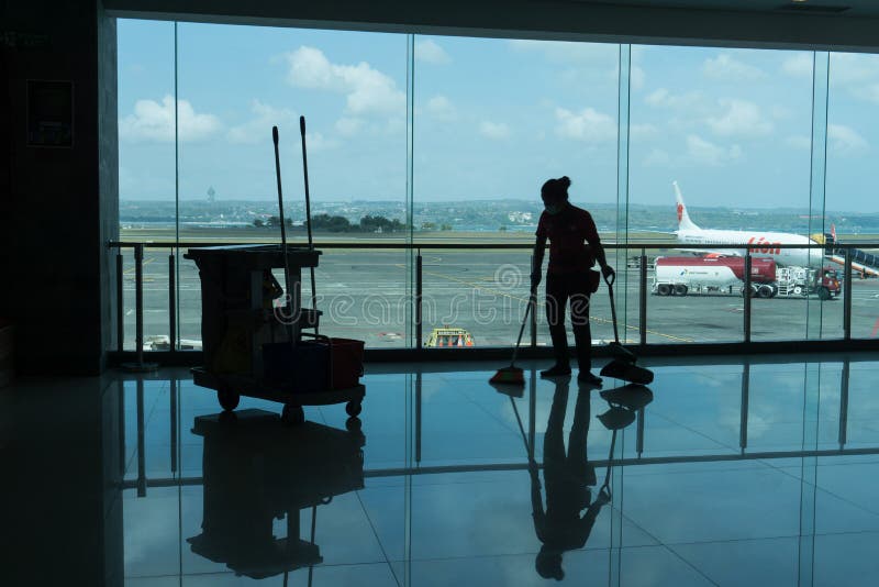 BADUNG/BALI- 28 MARS 2019 : la silhouette d'un portier nettoie le plancher terminal de départ avec le fond et l'airpo d'avion photo libre de droits BADUNG/BALI- 28 MARS 2019 : la silhouette d'un portier nettoie le plancher terminal de départ avec le fond et l'airpo d'avion photo libre de droits