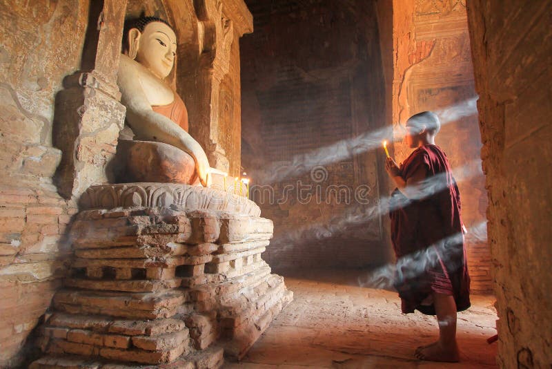 BAGAN, MYANMAR - May 2016: Monk burning candles in front of Buddha statue inside pagoda on May, 2016 in Bagan. Monks with light and Buddha are highlighted of Bagan. BAGAN, MYANMAR - May 2016: Monk burning candles in front of Buddha statue inside pagoda on May, 2016 in Bagan. Monks with light and Buddha are highlighted of Bagan.