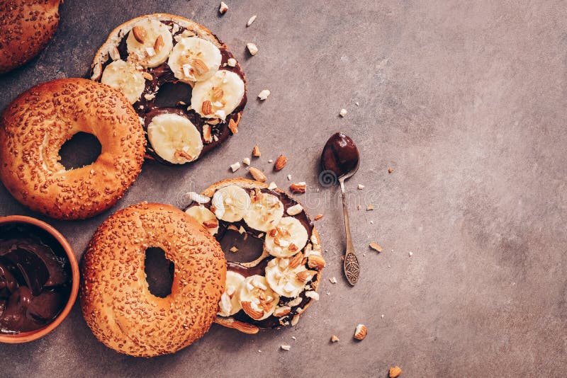 Bagel freschi con la crema, la banana ed i dadi del cioccolato su un fondo rustico scuro Vista superiore della prima colazione do fotografie stock Bagel freschi con la crema, la banana ed i dadi del cioccolato su un fondo rustico scuro Vista superiore della prima colazione do fotografie stock