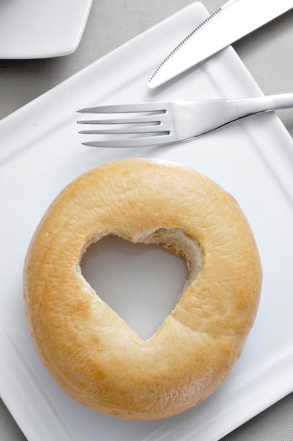 A plate with a plane bagel with a heart-shaped hole on a set table. A plate with a plane bagel with a heart-shaped hole on a set table