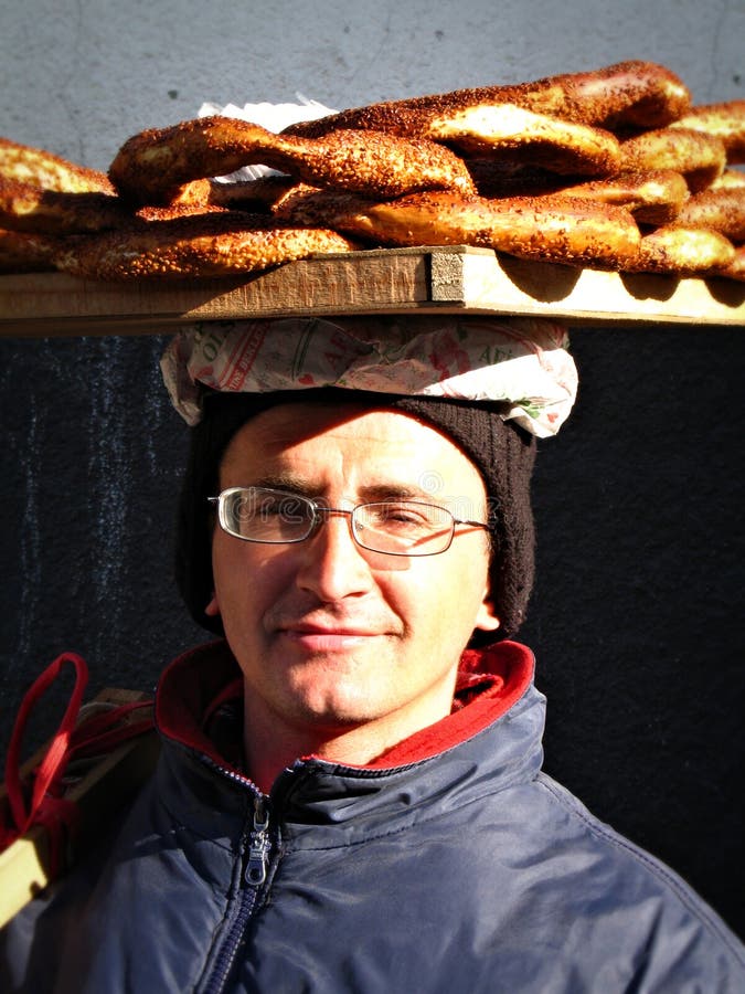 Ankara, Turkey - February, 20th 2007: Young bagel ('simit' in Turkish) seller poses for the camera with great enthusiasm on a sunny winter day at the neighborhood of Ankara citadel. A'simit' is a circular bread with sesame seeds, very common in Turkey, as well as in Greece, Balkans and Middle East. In Turkey'simit' is often sold by street vendors, who carry the simit in a tray on their head. Food vendor sold stock images, royalty-free photos and pictures