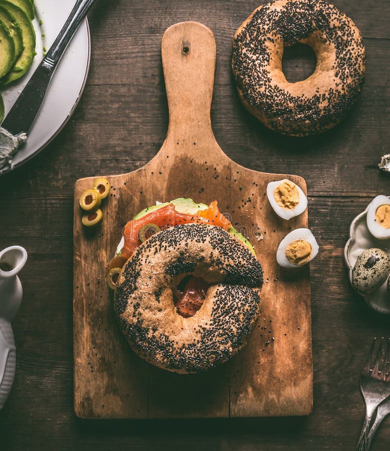 Bagel το ψωμί στον τέμνοντα πίνακα που ολοκληρώθηκε με το σολομό, αβοκάντο, μαγείρεψε τα αυγά ορτυκιών και το φρέσκο τυρί στοκ φωτογραφίες με δικαίωμα ελεύθερης χρήσης Bagel το ψωμί στον τέμνοντα πίνακα που ολοκληρώθηκε με το σολομό, αβοκάντο, μαγείρεψε τα αυγά ορτυκιών και το φρέσκο τυρί στοκ φωτογραφίες με δικαίωμα ελεύθερης χρήσης