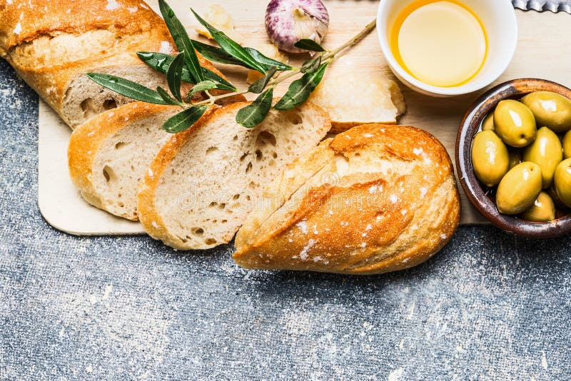 Baguette cut in slices on wooden chopping board, Olives , garlic and cheese on rustic background