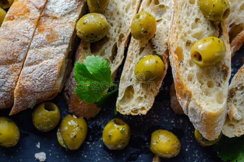 Baguette imbottita di olive tagliate con olive verdi fresche e prezzemolo servito su una piastra di pietra.
