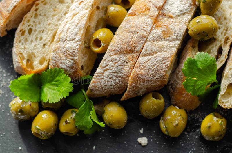Baguette imbottita di olive tagliate con olive verdi fresche e prezzemolo servito su una piastra di pietra immagini stock libere da diritti
