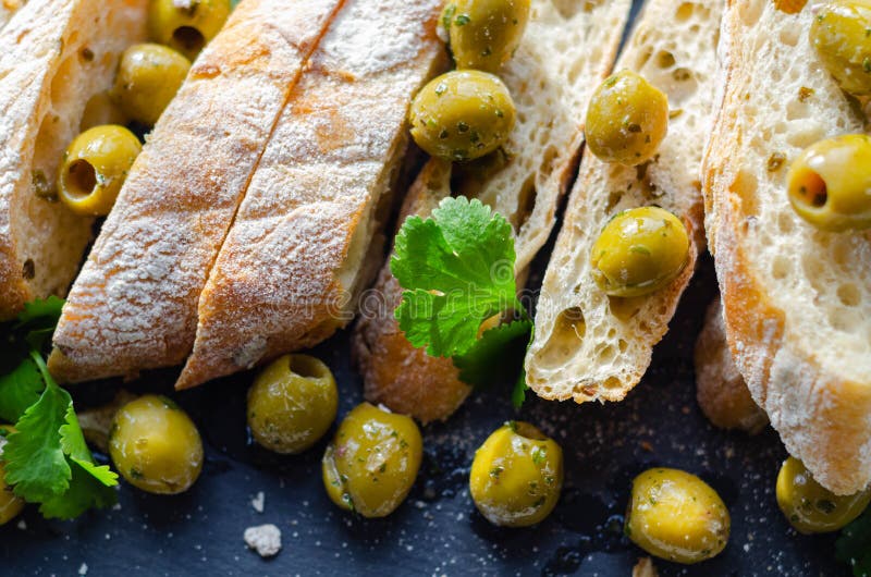 Baguette imbottite di olive, tagliate con olive verdi fresche e prezzemolo, servite su una piastra di pietra immagini stock libere da diritti