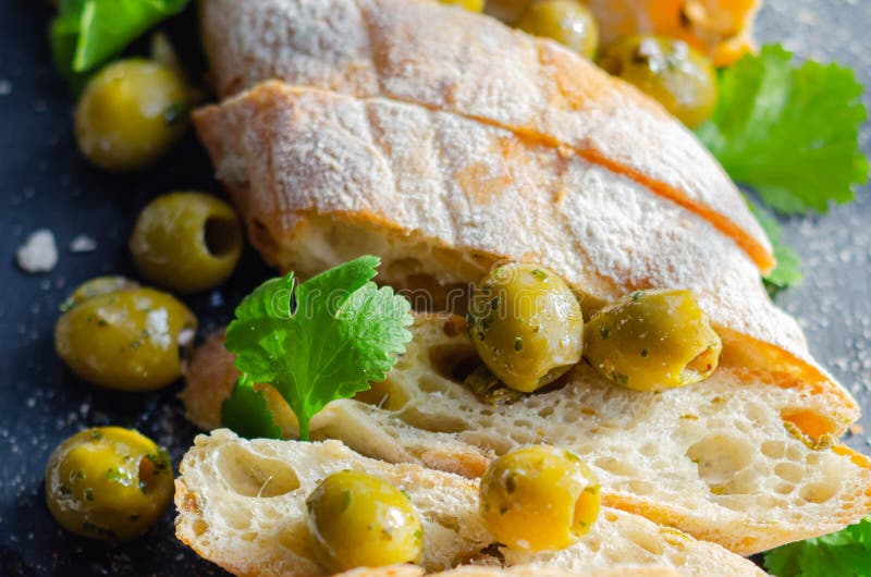 Baguette imbottite di olive, tagliate con olive verdi fresche e prezzemolo, servite su una piastra di pietra fotografia stock