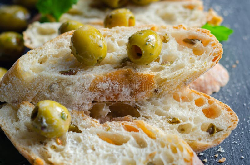 Baguette imbottite di olive, tagliate con olive verdi fresche e prezzemolo, servite su una piastra di pietra fotografia stock libera da diritti